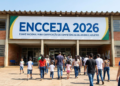 Grupo de adultos e crianças caminha em direção à entrada de escola com faixa ENCCEJA 2026.
