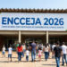 Grupo de adultos e crianças caminha em direção à entrada de escola com faixa ENCCEJA 2026.