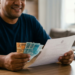 Homem sorridente confere documento e cédulas de real brasileiro.