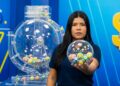 Mulher segura globo transparente com bolas numeradas coloridas em estúdio de loteria azul