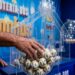 Mão masculina pegando bolas de sorteio douradas e brancas numeradas em globo de acrílico da Loteria dos Sonhos