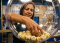 Mulher retira bola numerada de globo transparente em sorteio da Loteria do Ceará em Fortaleza, com painel azul ao fundo