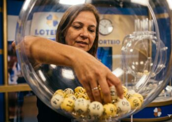 Mulher retira bola numerada de globo transparente em sorteio da Loteria do Ceará em Fortaleza, com painel azul ao fundo