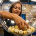 Mulher retira bola numerada de globo transparente em sorteio da Loteria do Ceará em Fortaleza, com painel azul ao fundo
