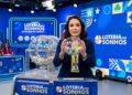 Apresentadora segura globo com bolas numeradas durante sorteio da Loteria dos Sonhos em estúdio azul