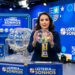 Apresentadora segura globo com bolas numeradas durante sorteio da Loteria dos Sonhos em estúdio azul