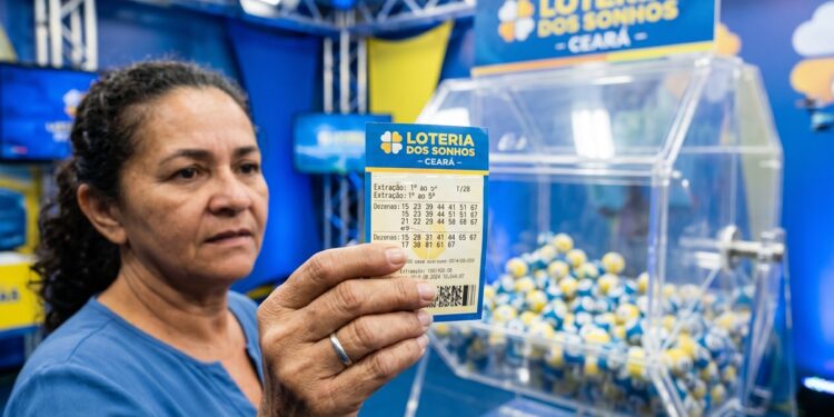 Mulher segura bilhete da Loteria dos Sonhos Ceará com dezenas marcadas, ao fundo globo de sorteio com bolas azuis e amarelas