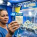 Mulher segura bilhete da Loteria dos Sonhos Ceará com dezenas marcadas, ao fundo globo de sorteio com bolas azuis e amarelas