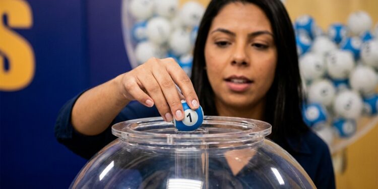 Mulher segura bola azul com número 1 sobre globo de acrílico com bolas coloridas ao fundo em sorteio