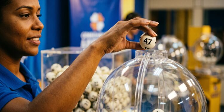 Mulher de camisa azul segura bola branca número 47 sobre globo de sorteio com diversas bolas numeradas
