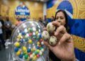 Mulher segura bolas com bichos e números sorteados da Loteria dos Sonhos, ao lado do globo colorido da LOTECE