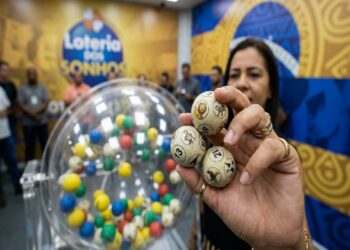 Mulher segura bolas com bichos e números sorteados da Loteria dos Sonhos, ao lado do globo colorido da LOTECE