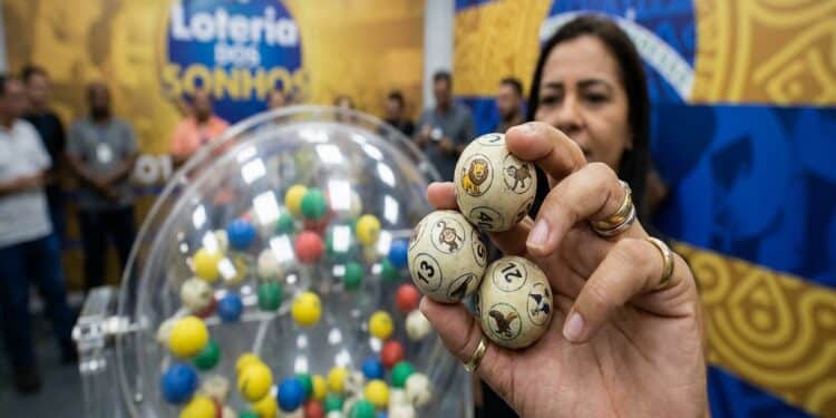 Mulher segura bolas com bichos e números sorteados da Loteria dos Sonhos, ao lado do globo colorido da LOTECE