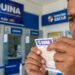 Homem de meia-idade segura e observa bilhete da Quina em frente ao guichê de lotérica da Caixa