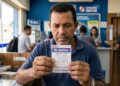 Homem de camisa azul segura bilhete da Quina, concurso 7838, com prêmio de R$ 12 milhões em casa lotérica