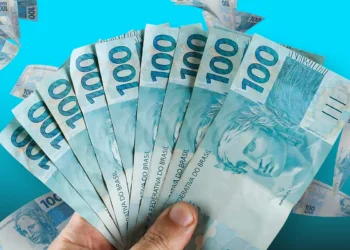 Leque de notas de R$ 100,00 brasileiros em fundo azul turquesa.
