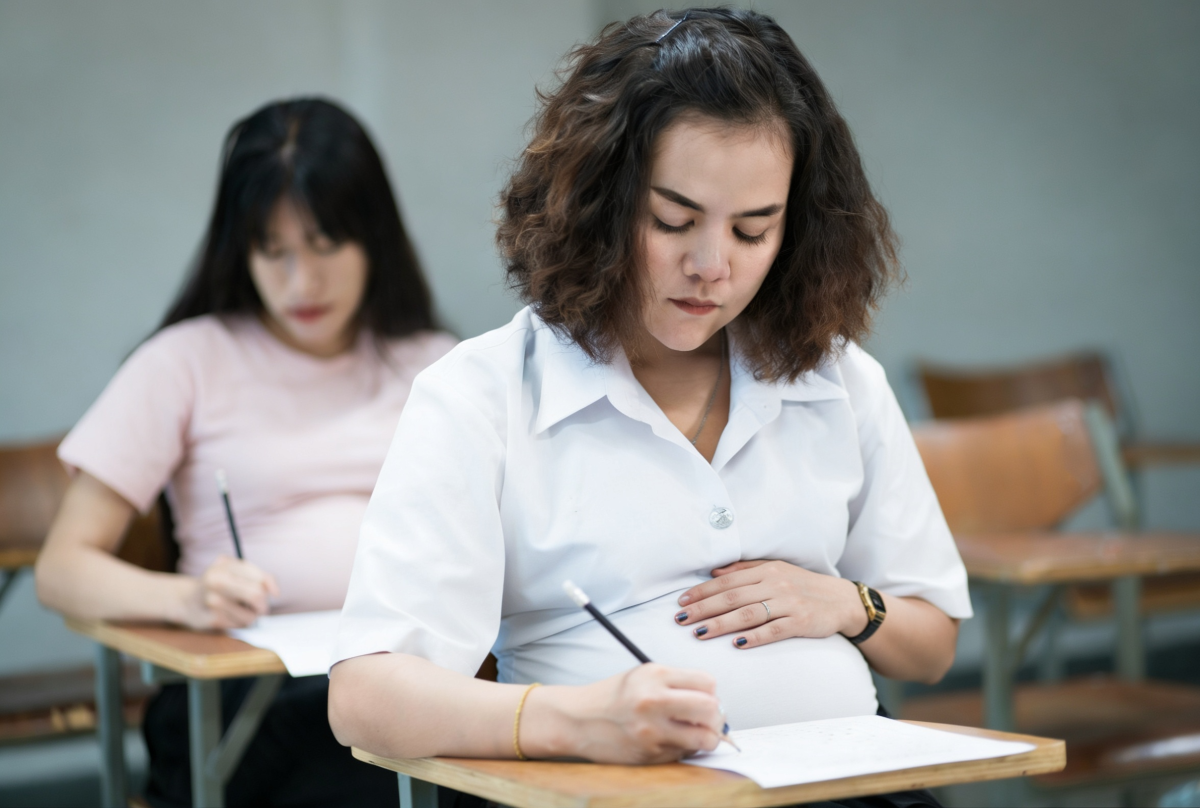 Estudante grávida concentrada realizando prova em sala de aula.