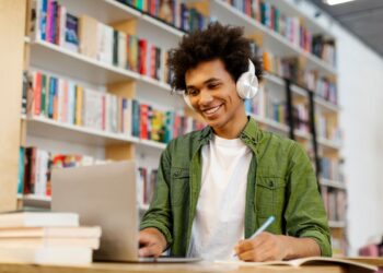 Estudante usando notebook e fones de ouvido enquanto aprende idiomas em uma biblioteca.