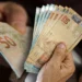 Mão segurando notas de R$ 50, representando previsão de aumento do salário mínimo nos próximos anos.