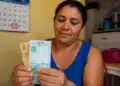 Mulher segurando cédulas de reais em ambiente doméstico, representando o pagamento final de maio do Bolsa Família.