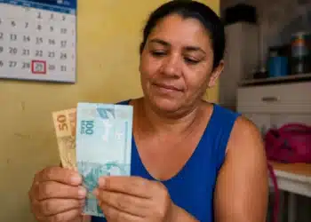 Mulher segurando cédulas de reais em ambiente doméstico, representando o pagamento final de maio do Bolsa Família.