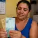Mulher segurando cédulas de reais em ambiente doméstico, representando o pagamento final de maio do Bolsa Família.