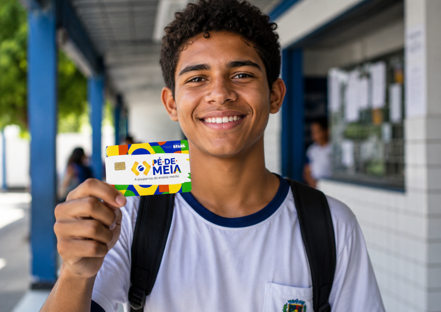 Jovem sorridente com camiseta escolar branca segura cartão Pé-de-Meia colorido em corredor de escola.