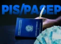 Carteira de Trabalho azul ao lado de cédulas de cem reais e mão segurando caneta com a sigla PIS/PASEP em destaque sobre fundo escuro