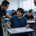 Jovem de camiseta azul sentado em carteira escolar sendo questionado por dois agentes de segurança uniformizados.