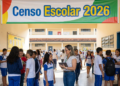Funcionária com tablet conversa com alunos de uniforme azul e branco no pátio de escola durante Censo Escolar 2026.