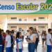 Funcionária com tablet conversa com alunos de uniforme azul e branco no pátio de escola durante Censo Escolar 2026.