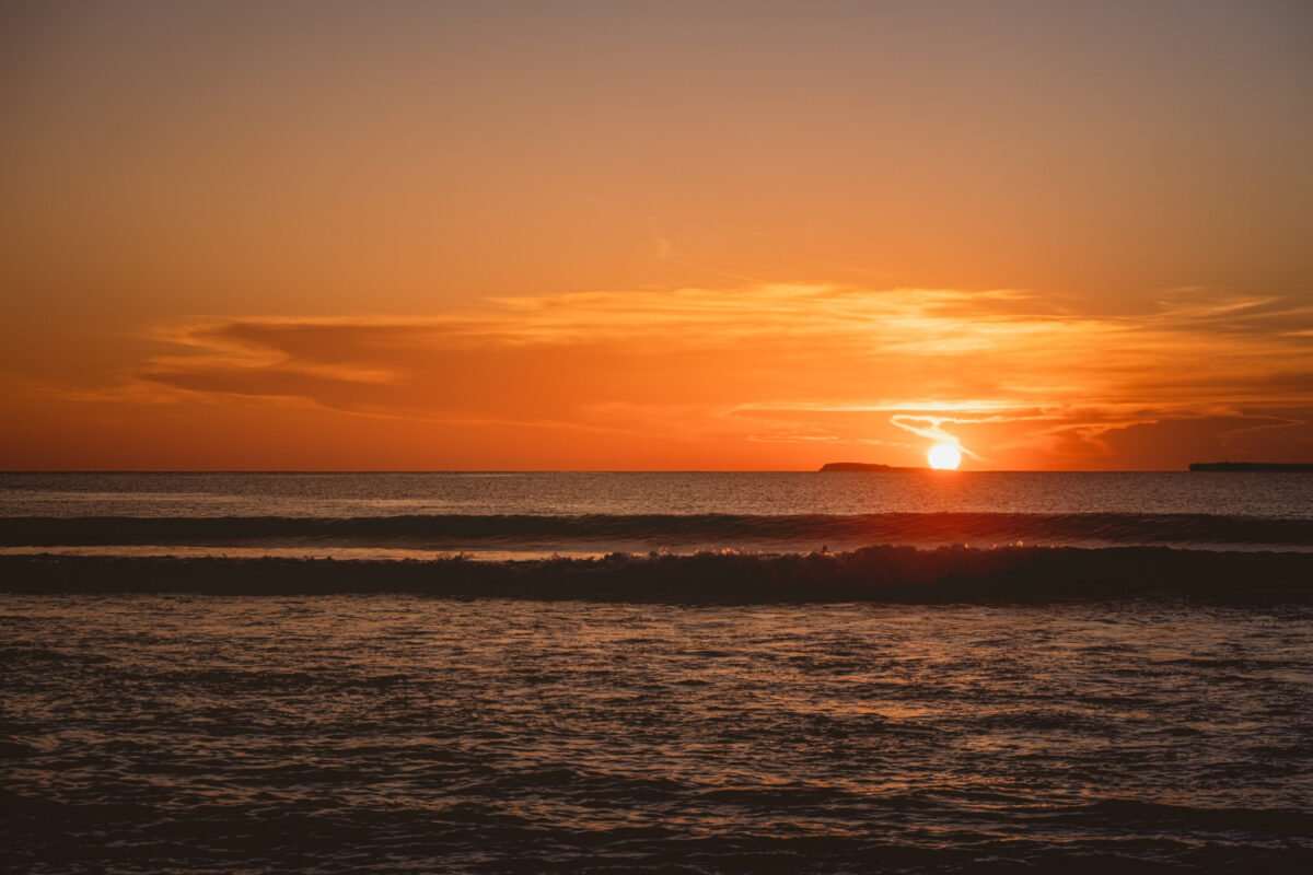 Sol alaranjado tocando o horizonte do mar com ondas em primeiro plano ao entardecer