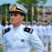 Oficial da Marinha de uniforme branco e quepe em destaque diante de formação militar enfileirada ao fundo em pátio externo