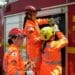 Bombeiras militares de Minas Gerais com uniforme operacional ajustam equipamentos ao lado de viatura