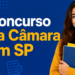 Jovem sorridente de blusa amarela segura cadernos com texto "Concurso da Câmara em SP" ao fundo azul.