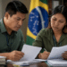 Dois profissionais indígenas com camisas verde-oliva revisam papéis em escritório com bandeira do Brasil ao fundo.