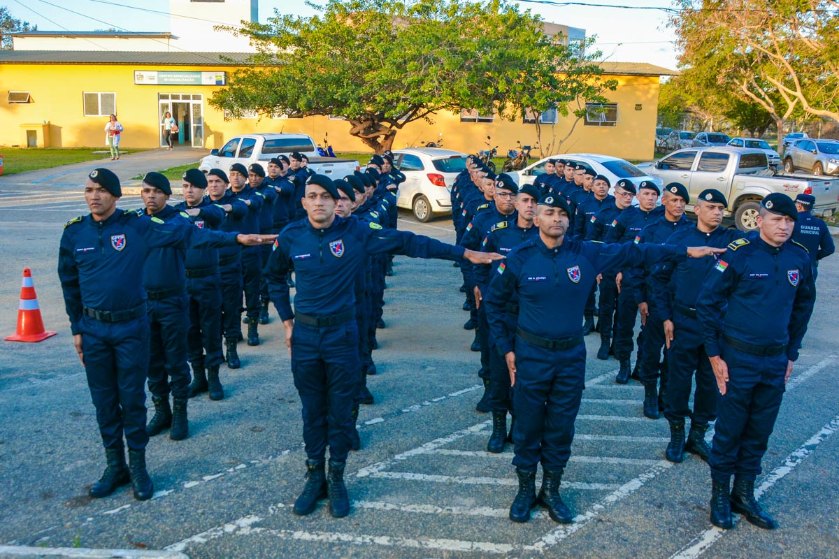 Agentes da Guarda Municipal com uniforme azul marinho e boina preta em formação, com braços estendidos durante cerimônia de juramento