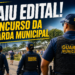 Agentes da Guarda Municipal com uniformes azuis e coletes patrulham a área externa com prédios ao fundo.
