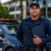 Guarda Civil Municipal fardado de azul marinho segurando prancheta preta ao lado de viatura com giroflex.