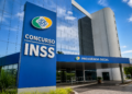 Prédio do INSS com fachada azul, placa de Concurso INSS e letreiro Previdência Social na entrada