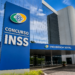 Prédio do INSS com fachada azul, placa de Concurso INSS e letreiro Previdência Social na entrada