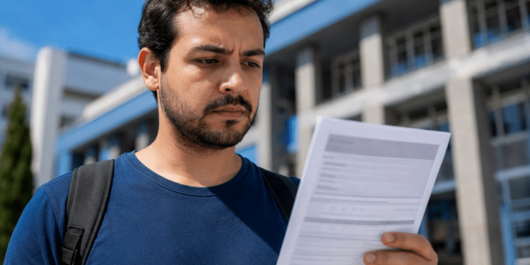 Jovem analisa documento de inscrição em concurso público diante de prédio institucional.