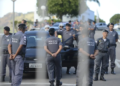 Policiais militares uniformizados em formação ao lado de viaturas durante operação ao ar livre