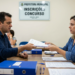 Homem de camisa azul entrega papéis a funcionária em setor de inscrições de concurso de prefeitura