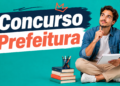 Jovem sentado com caderno e caneta, expressão pensativa, ao lado de pilha de livros e porta-lápis colorido