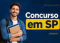 Jovem de barba curta segura cadernos, veste camisa jeans sobre camiseta branca com mochila preta nas costas