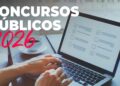Mãos digitando em laptop com lista de tarefas na tela, xícara de café ao lado, texto "Concursos Públicos 2026" em destaque