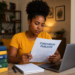 Mulher negra com camiseta amarela segura documento de Concursos Públicos, com livros e notebook na mesa.