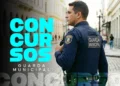 Guarda Municipal de uniforme azul-marinho com rádio comunicador patrulhando rua de paralelepípedos.