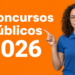 Mulher jovem de cabelos cacheados, óculos e camisa azul segurando pastas coloridas e apontando para texto de concursos